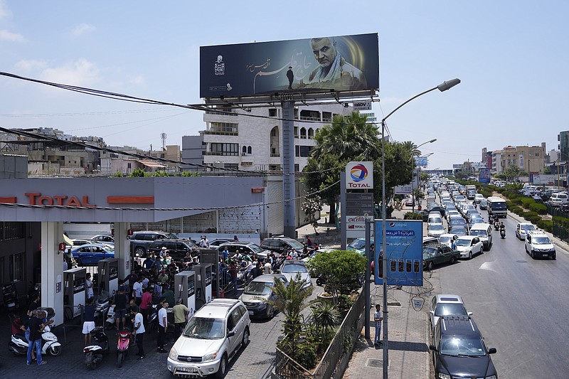 Drivers wait in a long line to get fuel at a gas station under a billboard showing Iranian Revolutionary Guard Gen. Qassem Soleimani, who was killed in Iraq in a U.S. drone attack in early January 2020, along the airport highway, in the southern suburbs of Beirut, Lebanon, Sunday, June 27, 2021. On Friday, Hassan Diab, Lebanon's caretaker prime minister, granted his approval to allow the financing of fuel imports at a rate higher than the official exchange rate, effectively reducing critical fuel subsidies that have been in place for decades, amid worsening gasoline shortages. (AP Photo/Hassan Ammar)