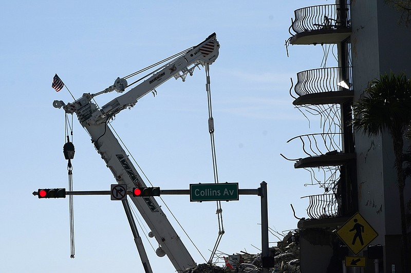 An American flag flies from a crane next to the Champlain Towers South condo building, where scores of victims remain missing more than a week after it partially collapsed, Sunday, July 4, 2021, in Surfside, Fla. Demolition teams are preparing to bring down the unstable remainder of the structure ahead of a tropical storm. (AP Photo/Lynne Sladky)