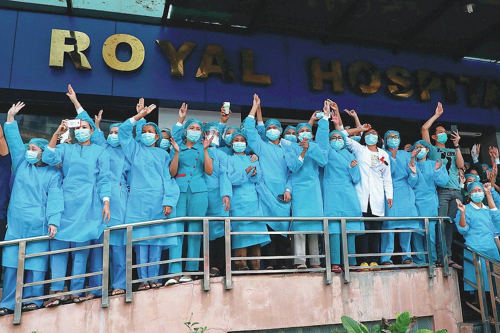 FILE - In this Sunday, Feb. 7, 2021 file photo, medical workers give the three-fingered salute outside Asia Royal Hospital as they watch protesters march in Yangon, Myanmar. Medics are particularly feared by the military because they are highly respected and well-organized, with a strong network of unions and professional groups. (AP Photo/File)