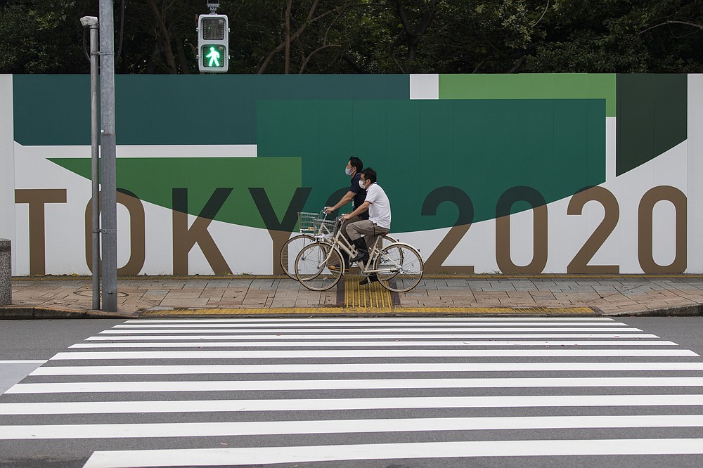 In this July 1, 2021, file photo, men cycle along the wall installed to close off a park being prepared for the Olympics and Paralympics Games in Tokyo. The pandemic-delayed Tokyo Olympics are shaping up as a TV-only event with few fans — if any — being allowed when they open in just over two weeks. Japan's Asahi newspaper, citing multiple unidentified government sources, says the opening ceremony will be limited only to VIP guests. (AP Photo/Hiro Komae, File)
