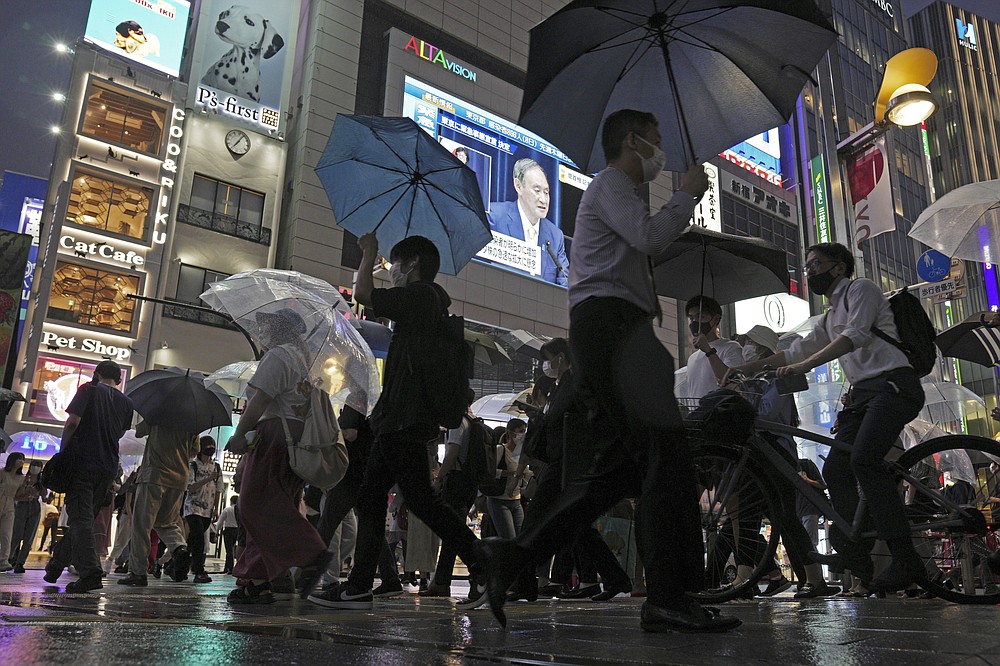 Pedestrians walk past a giant public TV with a live broadcast of a news conference by Japanese Prime Minister Yoshihide Suga after he announced a state of emergency because of rising coronavirus infections Thursday, July 8, 2021, in Tokyo. Suga said the state of emergency would go in effect on Monday and last through Aug. 22. This means the Olympics, opening on July 23 and running through Aug. 8, will be held entirely under emergency measures. The Paralympics open on Aug. 24. (AP Photo/Eugene Hoshiko)