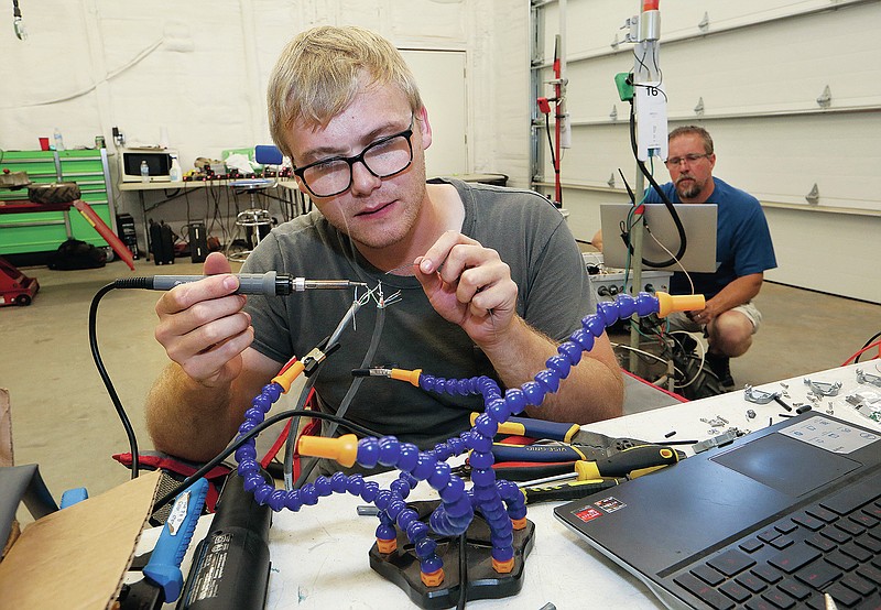 Nicholas Moehring, an electrical engineering intern from Wichita State University, solders while creating a wire harness for the robots as Andy Helten, right, senior engineer, works on a robot in the Greenfield Robotics shop near Cheney, Kan., on Tuesday, July 6, 2021. (Sandra J. Milburn/The Hutchinson News via AP)
