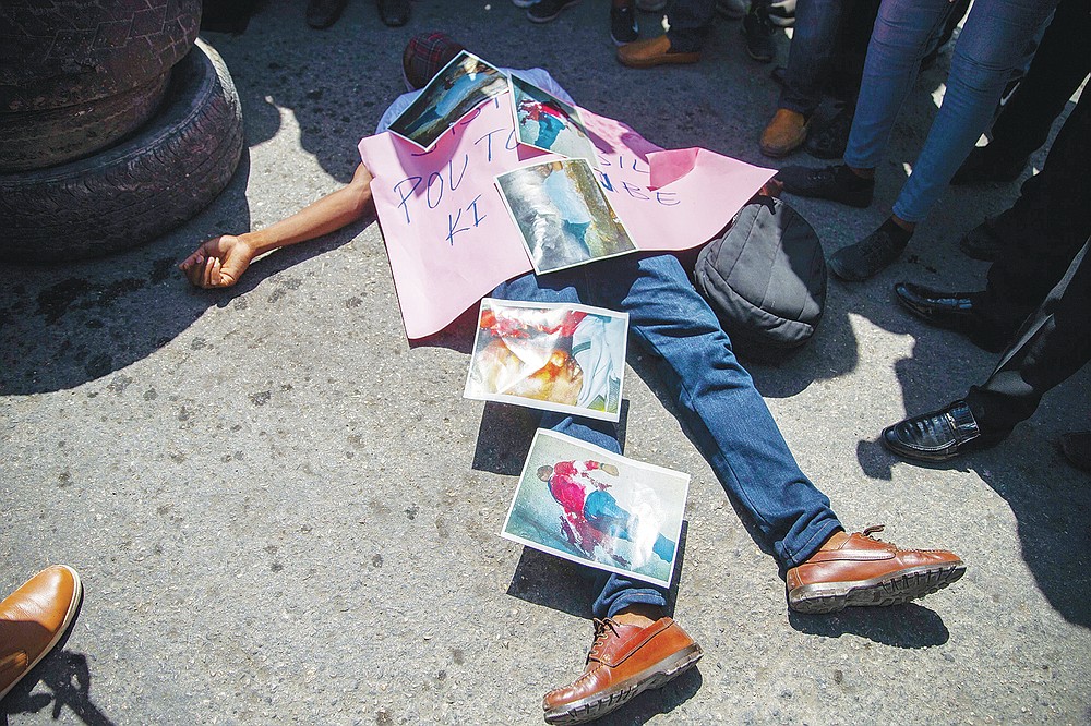 FILE - In this Sept. 1, 2020 file photo, a demonstrator lies on the pavement imitating the lifeless body of Bar Association President Monferrier Dorval, covered with photos of the murder scene, during a protest to demand justice for Dorval, who was fatally shot in Port-au-Prince, Haiti. On Friday, July 9, 2021, The Associated Press reported on claims circulating online wrongly asserting that a photo of a man lying on the pavement in blue pants covered in blood shows Haitian president Jovenel Moïse after his assassination early Wednesday. The photo is really from the Aug. 29, 2020, killing of Dorval, a prominent lawyer who was shot outside his home. (AP Photo/Dieu Nalio Chery, File)
