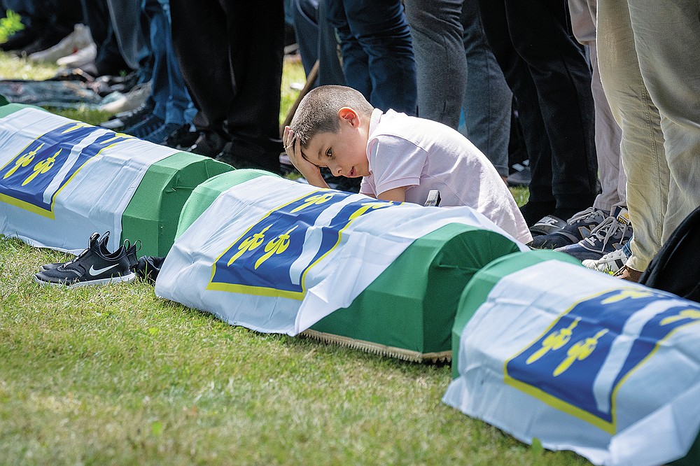 A boy reacts as mourners prepare for the funeral of newly identified victims at the memorial cemetery in Potocari near Srebrenica, Bosnia, Sunday, July 11, 2021. Bosnia is marking the 26th anniversary of the Srebrenica massacre, the only episode of its 1992-95 fratricidal war that has been declared a genocide by international and national courts. The brutal execution of more than 8,000 Muslim Bosniaks by Bosnian Serb troops is being commemorated by a series of events Sunday. (AP Photo/Darko Bandic)