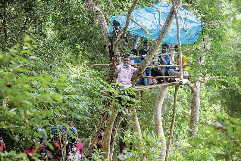 Sri Lankan teacher Ajith Attenayake holds his mobile phone as he uses it to share online lessons with students  from a tree house on a mountain in a reserve forest in Lunugala, Sri Lanka, July 3, 2021. Climbing rocks and sitting on tree tops is not part of their curriculum but children in villages surrounding the capital city are doing just that to be able to catch mobile signals to access their online classes. The digital divide fueled by uneven internet access and high data cost has forced many students out of the formal education system in Sri Lanka. (AP Photo/Eranga Jayawardena)