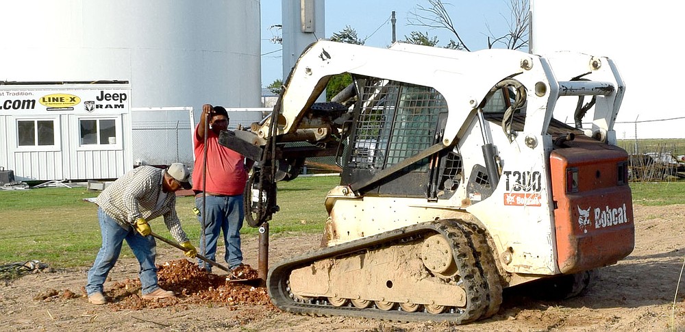 Westside Eagle Observer/MIKE ECKELS
Workers clear away dirt as a hydraulic drill attached to a Bobcat skid loader digs holes for the footing for the new bleachers at Bulldog Stadium in Decatur July 14.