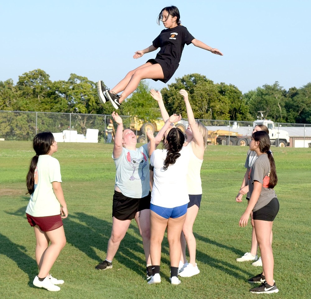 Westside Eagle Observer/MIKE ECKELS
McKenzie Thao (top) does a dismount from a prep stunt during the July 13 Decatur cheer team practice at Bulldog Stadium in Decatur. At present, the cheer team, volleyball and boys and girls basketball are all preparing for the 2021-22 sports season.