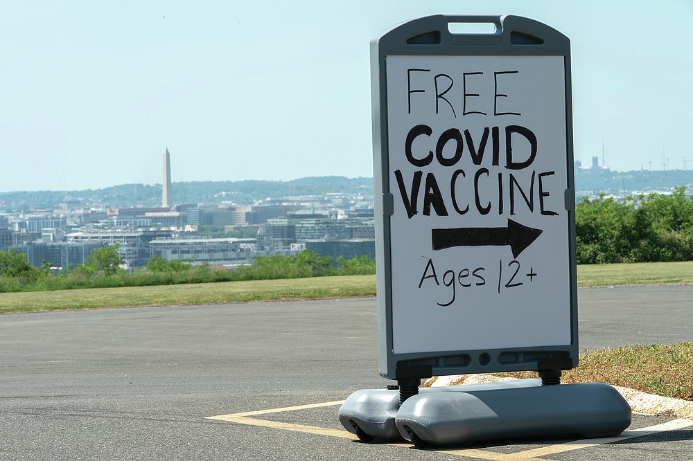 FILE - In this Wednesday, May 19, 2021 file photo, downtown Washington and the Washington Monument are seen behind a sign adverting a free vaccine drive with Pfizer COVID-19 vaccinations for members of the community 12 years and up outside a school in southeast Washington. On Friday, July 16, 2021, The Associated Press reported on stories circulating online incorrectly asserting President Joe Biden’s administration introduced a door-to-door campaign to offer COVID-19 vaccines as a way to confiscate guns or Bibles. But the vaccine campaign does not involve federal workers, it relies on local officials, private sector workers and volunteers to go into areas where there are lower vaccination rates and provide information on where to access the vaccine. (AP Photo/Jacquelyn Martin, File)