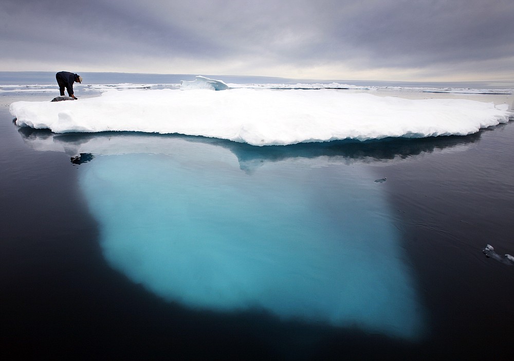 FILE - In this file photo dated July 2007, an Inuit seal hunter touches a dead seal atop an iceberg near Ammassalik Island, Greenland. The left-leaning government on Greenland which could be sitting on vast amounts of oil, has decided to suspend all oil exploration, Friday July 16, 2021, calling it “a natural step” because the Arctic government “takes the climate crisis seriously.” (AP Photo/John McConnico, FILE)