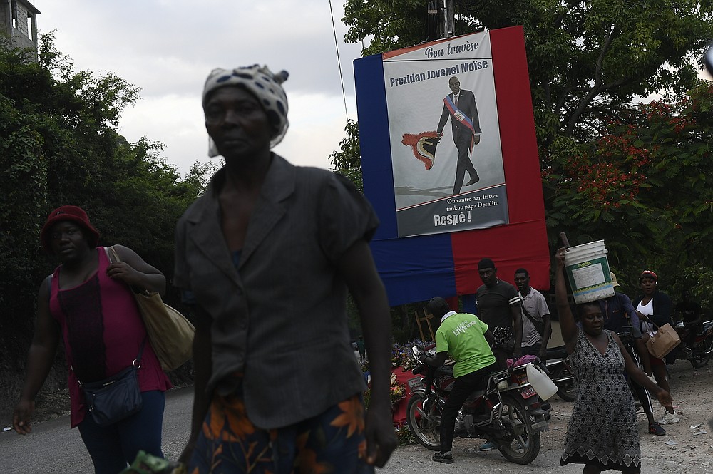 People walk near a poster featuring President Jovenel Moise in Port-au-Prince, Haiti, Saturday, July 17, 2021, ten days after Moise was assassinated in his home on July 7. (AP Photo/Matias Delacroix)