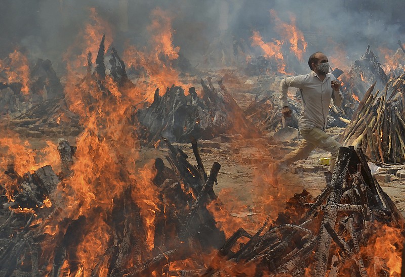 FILE - In this April 29, 2021, file photo, a man runs to escape heat emitting from the multiple funeral pyres of COVID-19 victims at a crematorium in the outskirts of New Delhi, India. India's excess deaths during the pandemic could be a staggering 10 times the official COVID-19 toll, likely making it modern India's worst human tragedy, according to the most comprehensive research yet on the ravages of the virus in the south Asian country. (AP Photo/Amit Sharma, File)