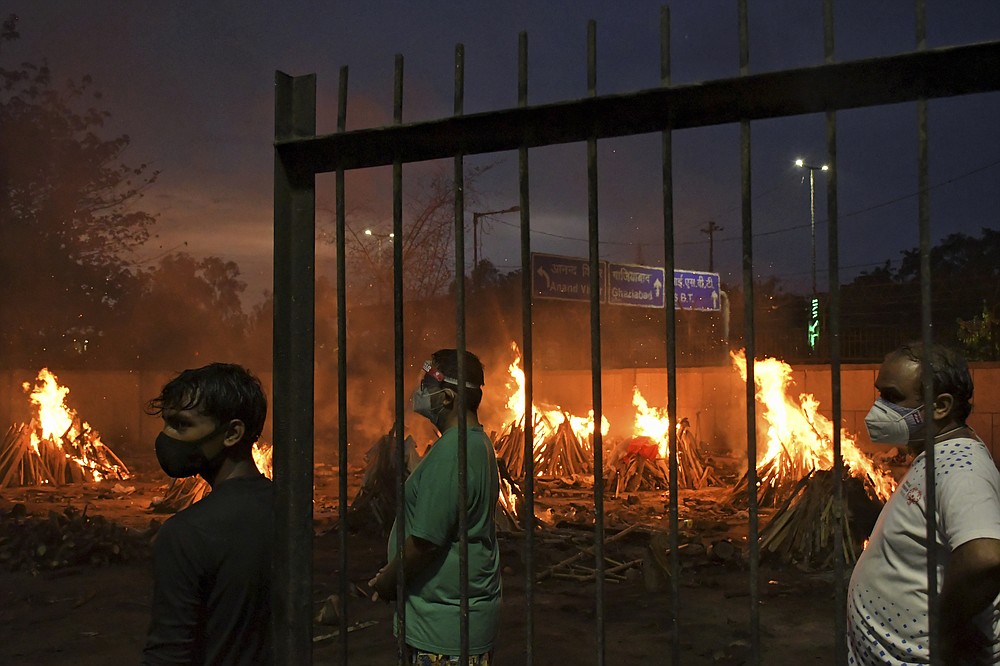 FILE - In this May 6, 2021, file photo, people watch burning funeral pyres of their relatives who died of COVID-19 in a ground that has been converted into a crematorium in New Delhi, India. India's excess deaths during the pandemic could be a staggering 10 times the official COVID-19 toll, likely making it modern India's worst human tragedy, according to the most comprehensive research yet on the ravages of the virus in the south Asian country. (AP Photo/Ishant Chauhan, File)