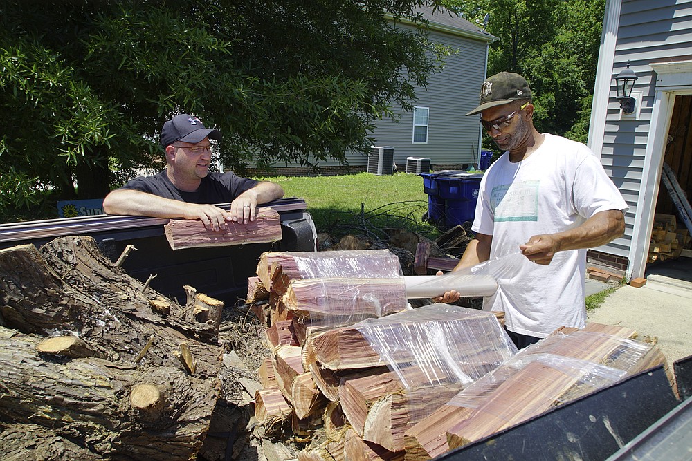 Alton Lucas, right, wraps firewood for sale as he and neighbor Ryan Isaac, a correctional officer, chat outside Lucas' home outside of Raleigh, N.C., on Friday, June 18, 2021. “I started the landscaping company, to be honest with you, because nobody would hire me because I have a felony,” said Lucas, whose business got off the ground with the help of Inmates to Entrepreneurs, a national nonprofit assisting people with criminal backgrounds by providing practical entrepreneurship education. (AP Photo/Allen G. Breed)