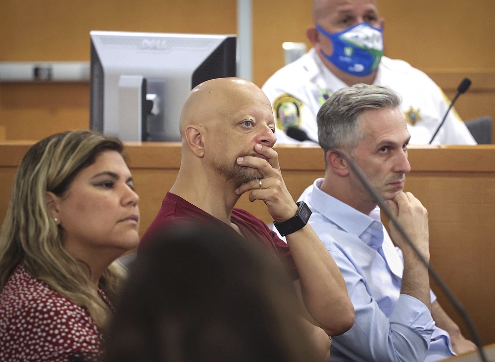 Champlain Towers South tenants Yadira Santo, from left to right, Paolo Longobardi and Oren Cytrynbaum listen closely as other residents share their grief and thoughts regarding the future of the site via Zoom, during a hearing, Wednesday, July 21, 2021, in Miami. Judge Michael Hanzman said victims and families who suffered losses in the collapse of the 12-story oceanfront Florida condominium will get a minimum of $150 million in compensation initially. (Carl Juste/Miami Herald via AP, Pool)