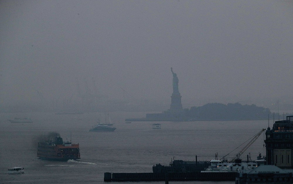 The Staten Island Ferry departs from the Manhattan terminal through a haze of smoke with the Statue of Liberty barely visible, Tuesday, July 20, 2021, in New York. Wildfires in the American West, including one burning in Oregon that's currently the largest in the U.S., are creating hazy skies as far away as New York as the massive infernos spew smoke and ash into the air in columns up to six miles high. (AP Photo/Julie Jacobson)