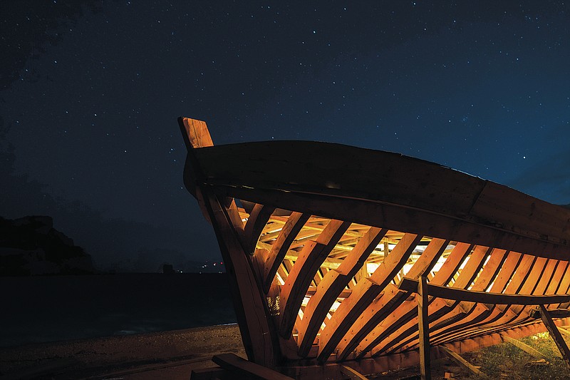 The frame of a traditional wooden boat stands under the night sky at Agios Isidoros boatyard one of the oldest on the eastern Aegean island of Samos, Greece, on Wednesday, June 9, 2021. But the art of designing and building these vessels, done entirely by hand, is under threat. Fewer people order wooden boats since plastic and fiberglass ones are cheaper to maintain. And young people aren’t as interested in joining a profession that requires years of apprenticeship, is physically and mentally draining and has an uncertain future.   (AP Photo/Petros Giannakouris)