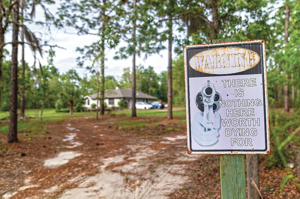 A sign featuring a pistol barrel pointed at would-be trespassers warns, "There is Nothing Here Worth Dying For" at the former home of Charles Newcomb, in Hawthorne, Fla., Thursday, April 15, 2021. Newcomb, the local KKK chapter's leader, known as the Exalted Cyclops, was involved in a 2015 murder plot against a former inmate at a prison where Newcomb once worked as a guard. (AP Photo/David Goldman)