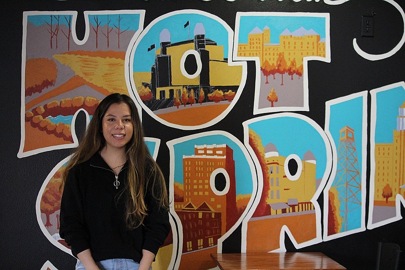 Capachi’s Coffee and Tea manager Allison Rubio stands in front of a Greetings from Hot Springs Mural in the store. Local coffee shops are being affected by multiple product shortages. - Photo by Krishnan Collins of The Sentinel-Record