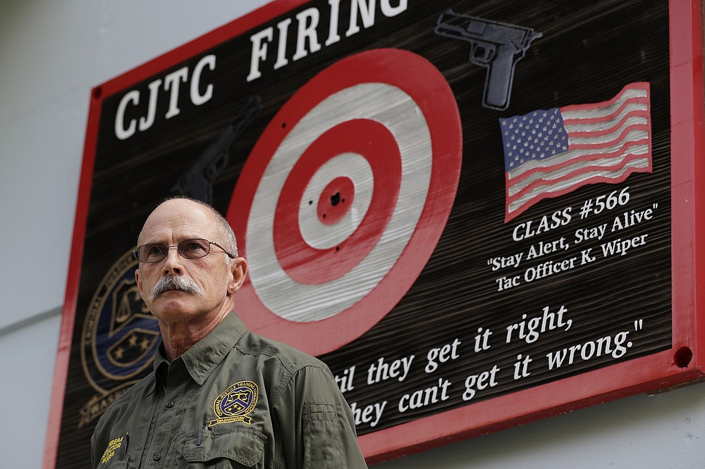 FILE - In this July 16, 2019, file photo, Doug Tangen, a firearms instructor at the Washington State Criminal Justice Training Commission, poses for a photo near a sign outside a firing range used in the state's Basic Law Enforcement Academy in Burien, Wash. Tangen says the facility has had trouble getting the supply of ammunition that they need for firearms training due to shortages blamed on the COVID-19 pandemic and record sales of firearms. (AP Photo/Ted S. Warren, File)