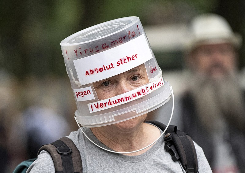 A demonstrator walks through Berlin-Charlottenburg with a plastic bucket placed on his head reading 'Absolutely safe against the stupidity virus', in Berlin, Sunday Aug. 1, 2021, during a protest against coronavirus restrictions. Hundreds have turned out in Berlin to protest the German government’s anti-coronavirus measures despite a ban on the gatherings, leading to arrests and clashes with police.  (Fabian Sommer/dpa via AP)