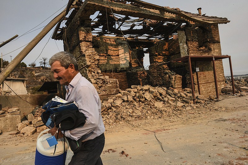 A man walks with some items he collected from the remains of his house in wildfire-destroyed Kalemli village near Manavgat, Antalya, Turkey, Monday, Aug. 2, 2021. For the sixth straight day, Turkish firefighters were battling Monday to control the blazes tearing through forests near Turkey's beach destinations. Fed by strong winds and scorching temperatures, the fires that began Wednesday have left eight people dead and forced residents and tourists to flee vacation resorts in a flotilla of small boats.(AP Photo)