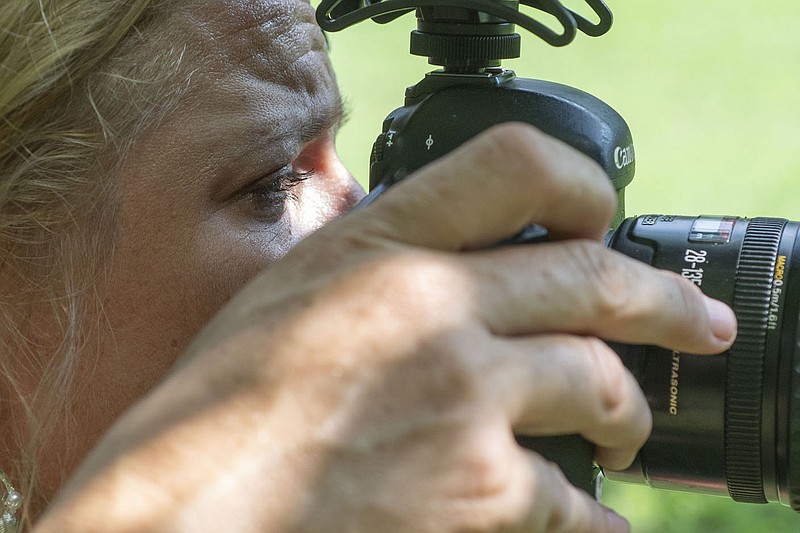 Diana Michelle of Fayetteville keeps her eyes on her camera while recording Paul Summerlin of Fayetteville as he performs some yoga poses Wednesday July 28, 2021 at Wilson Park in Fayetteville. (NWA Democrat-Gazette/J.T. Wampler)