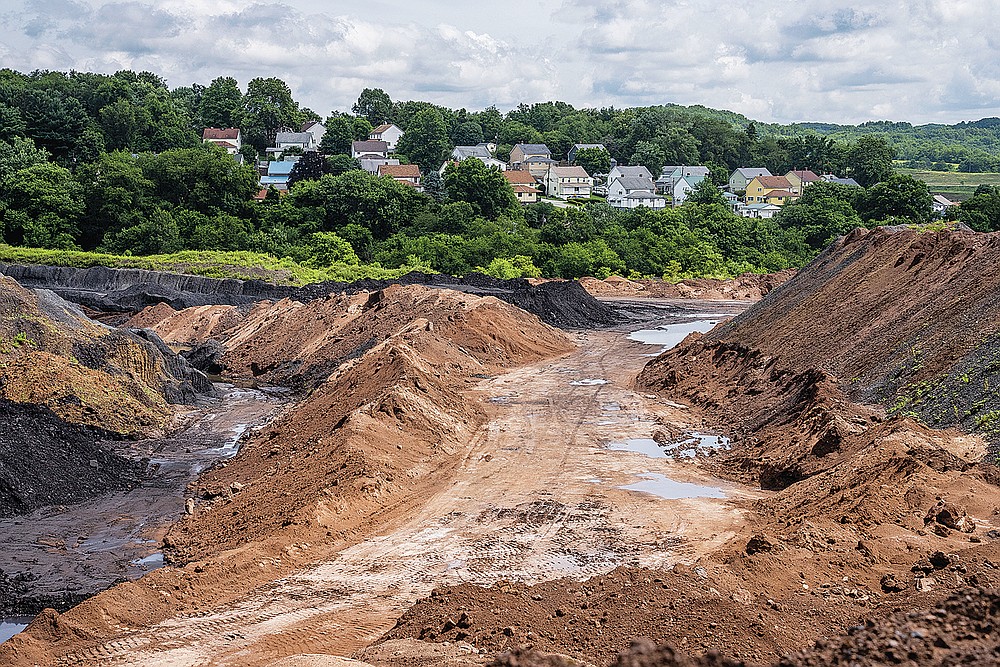Homes in a Russelton, Pa.,  neighborhood can be seen alongside a coal waste pile on Friday, July 23, 2021. The pile is being trucked to be used at the Scrubgrass Power plant in Venango County and later returned in the form of ash. (Andrew Rush/Pittsburgh Post-Gazette via AP)