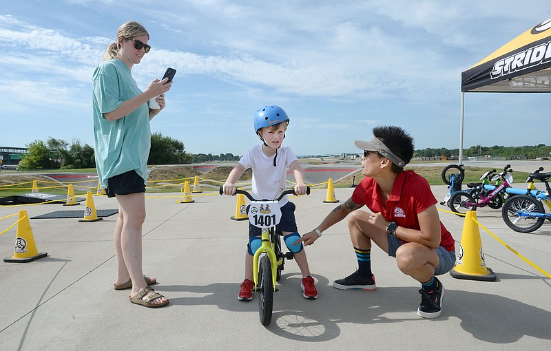 Melisa Jennings (from right), education and events manager for Strider bikes, offers some instruction and encouragement Thursday for Charlton White, 4, as his mother, Blaire White of Fayetteville, videos his first ride on a pedal bicycle during a youth riding clinic hosted by the Jones Center and Strider Bikes at Runway Bike Park in Springdale. 
(NWA Democrat-Gazette/Andy Shupe)