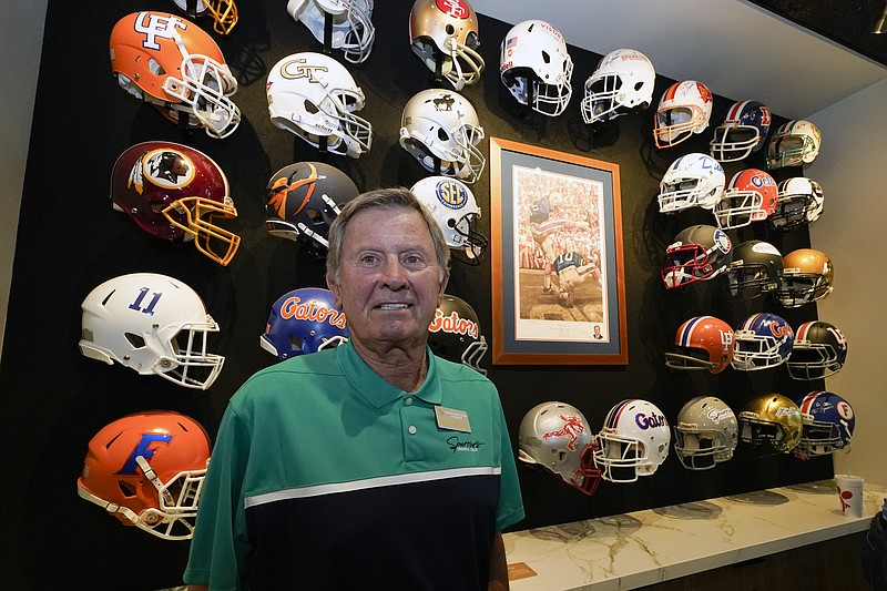 Steve Spurrier stands in front of a display of helmets of teams that he previously played for or coached at his new restaurant, the Gridiron Grill, Thursday, June 17, 2021, in Gainesville, Fla. The restaurant doubles as Spurrier's personal museum. (AP Photo/John Raoux)