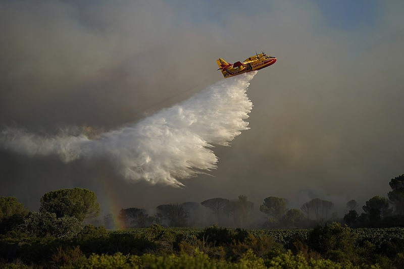 A water-dumping aircraft dumps water on a wildfire near Le Luc, southern France, Tuesday, Aug. 17, 2021. Thousands of people fled homes, campgrounds and hotels near the French Riviera on Tuesday as firefighters battled a blaze that raced through nearby forests, sending smoke pouring down wooded slopes toward vineyards in the picturesque area. (AP Photo/Daniel Cole)