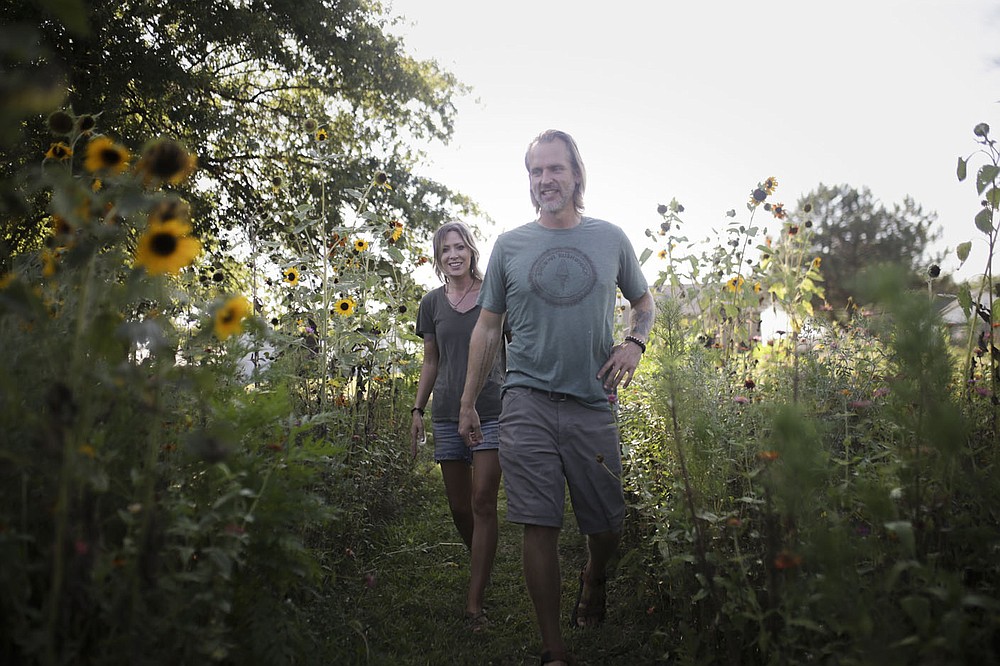 Caleb Schoeppe (center) and partner Sydney Sloan (left) walk past their stalks of sunflowers, Friday, August 27, 2021 at Sacred Hollow Farm in Lowell. The pandemic forced Caleb Schoeppe and his partner Sydney Sloan to take a hard look at their lives and they decided they didn't really like what they saw - so Caleb quit his corporate job, Sydney stopped styling hair, and they opened up a u-pick wildflowers business on their acreage. Check out nwaonline.com/210830Daily/ for today's photo gallery.
(NWA Democrat-Gazette/Charlie Kaijo)