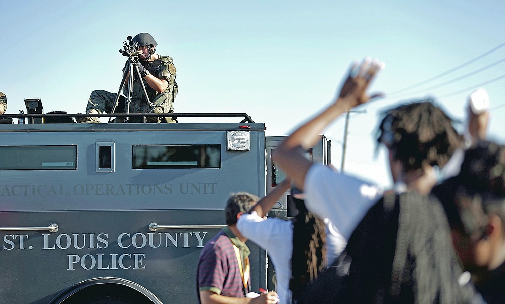 ADVANCE FOR PUBLICATION ON FRIDAY, SEPT. 10, AND THEREAFTER - FILE - In this Wednesday, Aug. 13, 2014 file photo, a member of the St. Louis County Police Department points his weapon in the direction of a group of protesters in Ferguson, Mo. On Saturday, Aug. 9, 2014, a white police officer fatally shot Michael Brown, a Black teenager, in the St. Louis suburb. (AP Photo/Jeff Roberson, File)