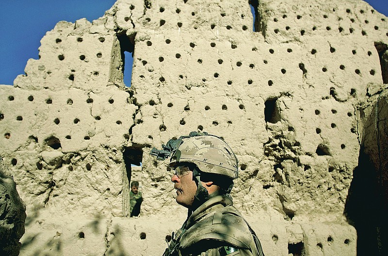 FILE - In this Nov. 22, 2006 file photo, a Canadian soldier, and a soldier from the Afghan National Army, behind wall, walk along a destroyed grape drying silo at the Canadian base near the town of Zhari in the Kandahar province of Afghanistan. The holes in the wall are for mounting sticks for drying grapes. (AP Photo/David Guttenfelder, File)