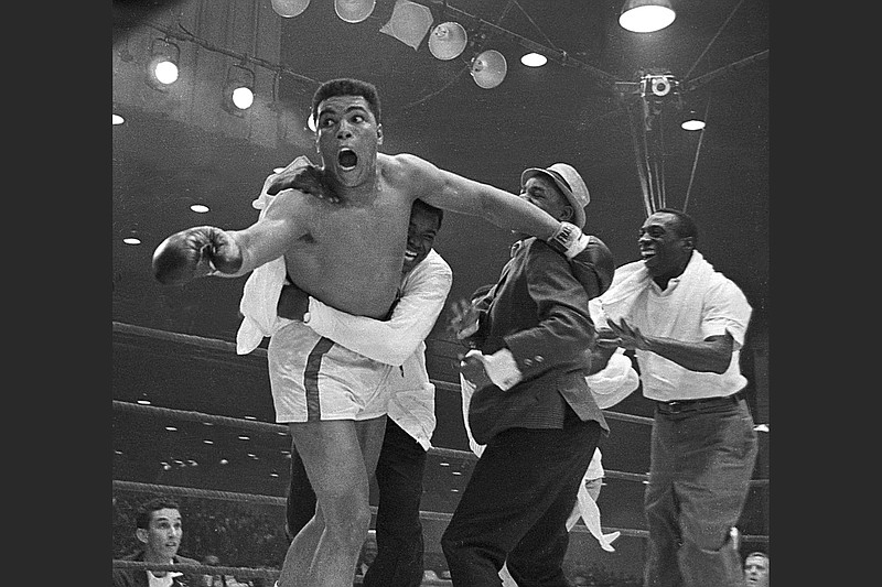 Cassius Clay’s handlers hold him back after he is announced the new heavyweight champion of the world after knocking out Sonny Liston on Feb. 25, 1965, in Miami. Bundini Brown embraces Ali. Luis Sarria runs to the group with a smile on the right. (Courtesy of PBS)