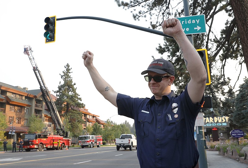 South Lake Tahoe firefighter Leo Gebhardt gestures to passing cars as they honk their horns along Highway 50 near Stateline, Nev., in South Lake Tahoe, Calif., Sunday, Sept. 5, 2021. Cal Fire officials downgraded some evacuation orders near Lake Tahoe and allowed thousands of South Lake Tahoe residents who fled the Caldor Fire last week to return home Sunday. (Jane Tyska/Bay Area News Group via AP)