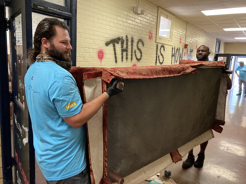 Justin Miller, (left) a Lowe's employee from Hot Springs, and Jermaine Blanchard, from the company's store in Searcy, haul off an old sofa Tuesday as they help get First Ward School ready to be renovated and turned into a homeless shelter. (Pine Bluff Commercial/Byron Tate)