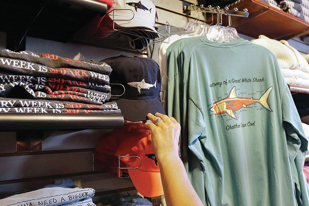 FILE— In this July 2, 2014 photo, a customer examines shark-themed clothing at a store in Chatham, Mass. Cape Cod is slowly embracing its shark reputation, three summers after the popular vacation destination saw its first great white shark attacks in generations. A growing group businesses are cashing in on the shark trend with retail offerings to tourists and charter boat operators giving visitors a chance to see the marine predators up close. (AP Photo/Steven Senne, File)