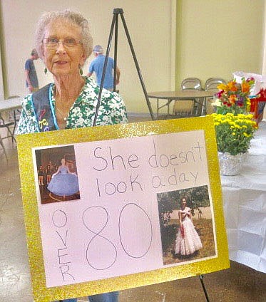 Westside Eagle Observer/SUSAN HOLLAND
Zanetta Bedwell poses beside a poster which greeted guests as they arrived at her surprise 80th birthday party. The poster featured two early day photos of Bedwell when she was a student at Gravette High School and others were featured in a slide show at the event.