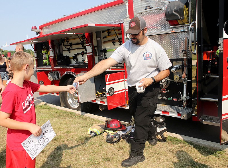 Capt. Heath Andrews with Farmington Fire Department hands a fire sticker to Hayden Stout, 8, of Farmington. The firefighters explained safety rules and shared information about the fire truck at the Farmington Fall Festival on Saturday.