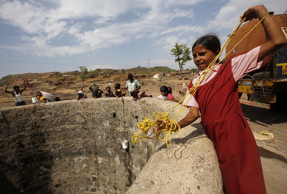FILE - In this May 4, 2016, file photo, a girl wearing her school uniform pulls a rope attached to a bucket as she tries to draw water after a tanker emptied water into a dried up well at Umber Maal village in Thane district in Maharashtra state, India. Climate change could push more than 200 million people to move within their own countries in the next three decades and create migration hotspots unless urgent action is taken in the coming years to reduce global emissions and bridge the development gap, a World Bank report has found. The report published on Monday, Sept. 13, 2021 examines how long-term impacts of climate change such as water scarcity, decreasing crop productivity and rising sea levels could lead to millions of what the report describes as “climate migrants” by 2050. (AP Photo/ Rajanish Kakade, File)