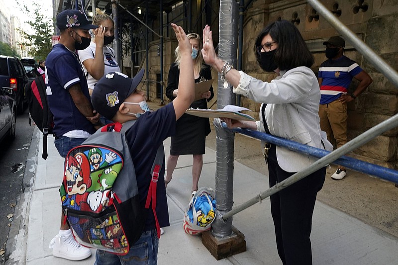 Wilfredo Padilla Jr., 7, a second-grader at PS811 in New York, gets a high-five from Alternative Assessment Coordinator Patricia Valentino, as he arrives for the first day of school, Monday, Sept. 13, 2021. School started Monday for about a million New York City public school students in the nation's largest experiment of in-person learning during the coronavirus pandemic. (AP Photo/Richard Drew)