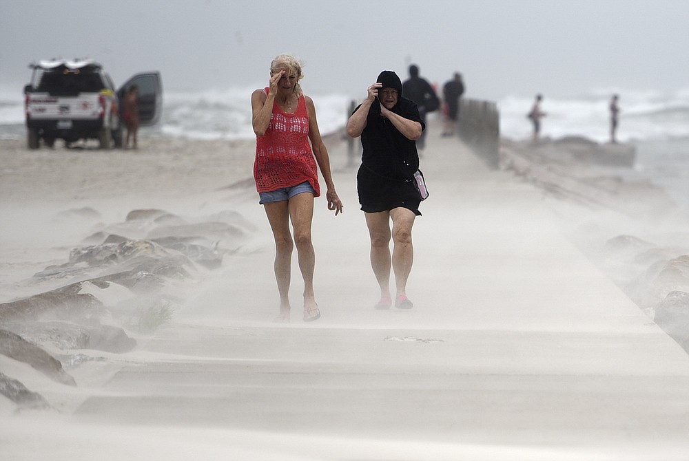 People shield their faces from wind and sand ahead of Tropical Storm Nicholas, Monday, Sept. 13, 2021, on the North Packery Channel Jetty in Corpus Christi, Texas. Lifeguards paroled the beach to warn people of the upcoming conditions. (Annie Rice/Corpus Christi Caller-Times via AP)