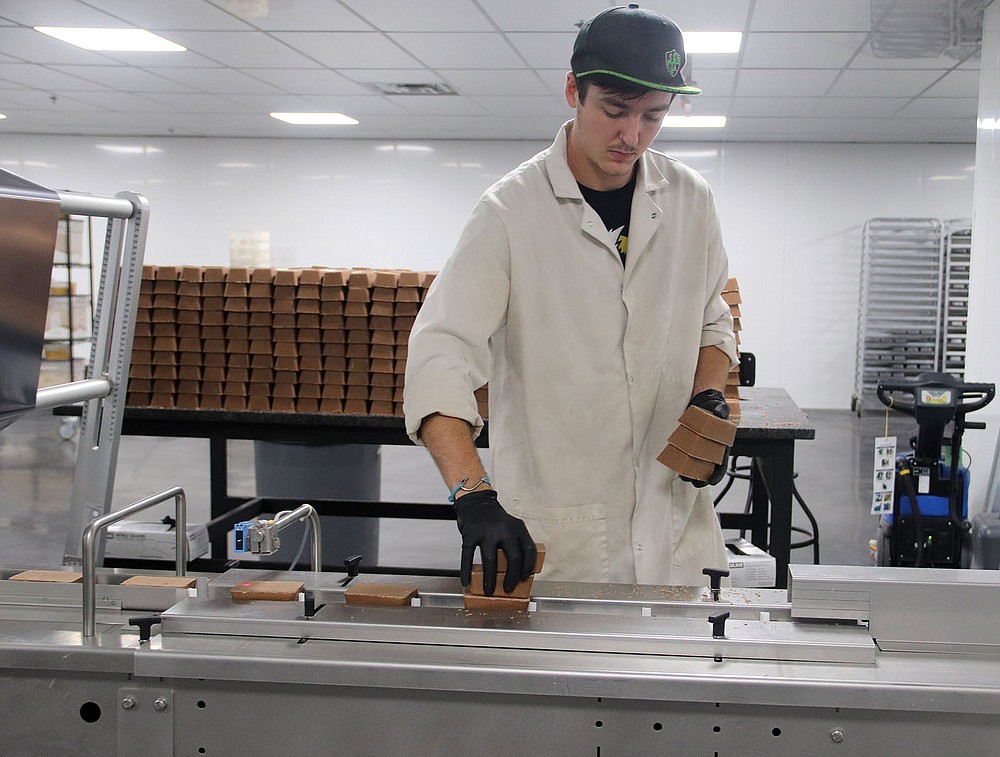 LYNN KUTTER ENTERPRISE-LEADER Layne Nikes places Keto Savage bars on a conveyer belt. The company produces the keto bars in the former Harps grocery store in Lincoln. The bars go from the conveyer belt into a machine that wraps the bars. From there, the bars are boxed and sent out.