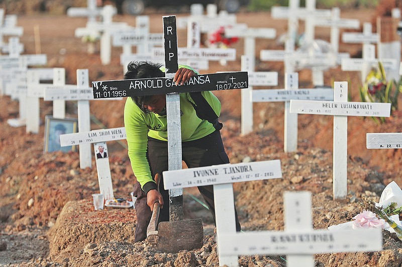 A worker fixes grave mark at Rorotan Cemetery which was reserved for those who died of COVID-19, in Jakarta, Indonesia, Wednesday, Aug. 25, 2021. Jakarta government cleared and dedicated the land at the cemetery for the victims of the virus in March, which helped to make space for thousands of people that were confirmed to have died from the virus during the deadly wave the country experienced over the summer this year. (AP Photo/Achmad Ibrahim)