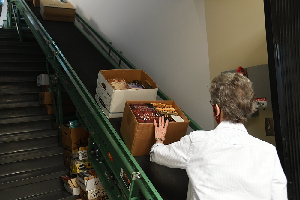 Peggy Young, Friends of the Library board president, loads donated books onto a conveyor belt to be sent to the top floor of the library. The books will be on sale Friday and Saturday during the library's annual book sale. - Photo by Tanner Newton of The Sentinel-Record