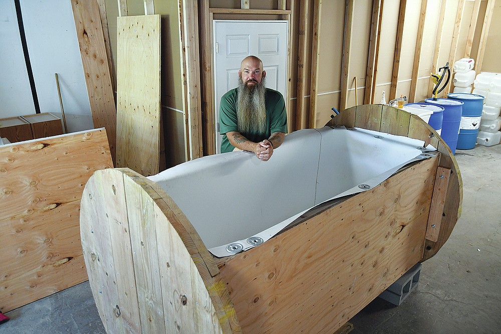 In this Wednesday, Aug. 11, 2021, photo, Seth Viddal, who co-owns The Natural Funeral, stands behind a nearly completed human body composting vessel in Arvada, Colo. On Sept. 7, Colorado became the second state after Washington to allow human body composting, and Oregon will allow the practice beginning next July. The vessel will be packed with wood chips and straw and will be able to compost a body in six months. About the size of a standard grave, the rectangular insulated wooden box is lined with waterproof roofing material and packed with wood chips and straw. Two large spool wheels on either end allow it to be rolled across the floor, providing the oxygenation, agitation and absorption required for a body to compost. (AP Photo/Thomas Peipert)