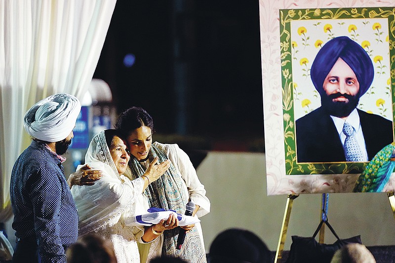 Valarie Kaur, right, of the Revolutionary Love Project, hugs Harjinder Kaur Sodhi, the widow of Balbir Singh Sodhi, middle, as Balbir's brother Rana Singh Sodhi, left, looks on at a memorial service on the 20th anniversary of the murder of Balbir Singh Sodhi Wednesday, Sept. 15, 2021, in Mesa, Ariz. Sikh businessman Balbir Singh Sodhi was helping plant a flower bed at his Arizona gas station when he was shot dead by a man seeking to avenge 9/11. Mistaken for an Arab Muslim because of his turban and beard, Sodhi was the first person to die in a wave of bias crimes unleashed by the attacks. (AP Photo/Ross D. Franklin)