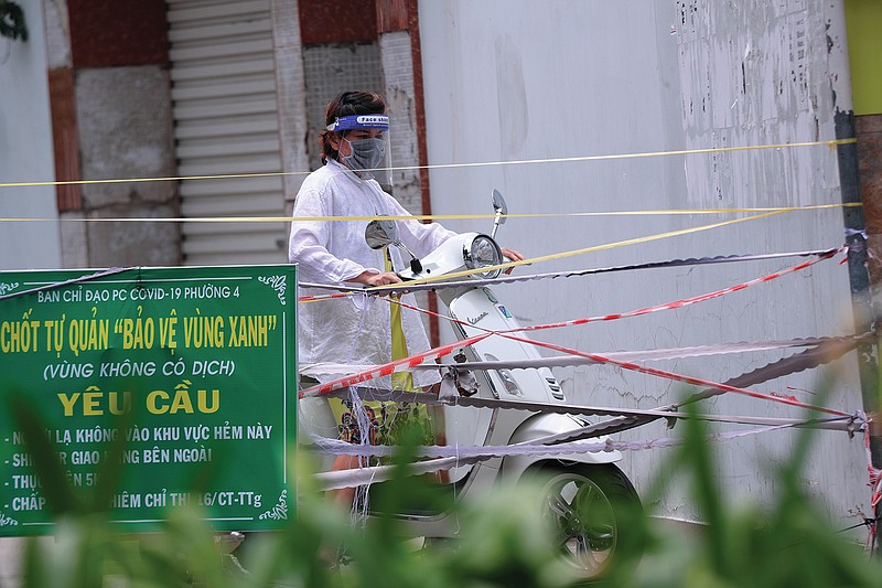 A woman stops her scooter as the alley is blocked with cordon tapes in Vung Tau, Vietnam, Monday, Sept. 13, 2021. The roadblocks and barricades make the streets of this southern Vietnamese city look like they did during the war that ended almost 50 years ago. But this time, the battle is being fought against the rampaging coronavirus.(AP Photo/Hau Dinh)