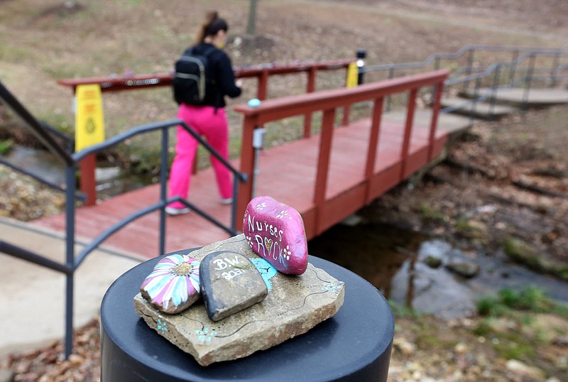 A medical staff member with Washington Regional Medical Center walks Jan. 27 past decorated rocks stacked near and on the hand rail of a foot bridge on the campus of the hospital in Fayetteville. The hospital announced plans to expand its campus west to the proposed Drake Farms mixed-use development west of Gregg Avenue. (File photo/NWA Democrat-Gazette/David Gottschalk)
