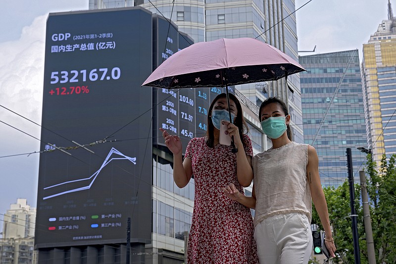 FILE - In this Aug. 24, 2021, file photo, women wearing face masks to help curb the spread of the coronavirus walk by an electronic billboard showing China's Gross Domestic Product (GDP) index on a commercial office building in Shanghai, China. Developing economies in Asia will likely grow at a slower pace than earlier expected due to prolonged COVID-19 outbreaks and uneven progress in vaccinations, the Asian Development Bank said in a report Wednesday, Sept. 22, 2021.( (AP Photo/Andy Wong, File)
